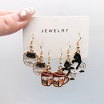 Three pairs of playful teacup cat earrings on a display card
