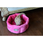 An orange kitten sits in an Armarkat Pink velvet cuddle bed