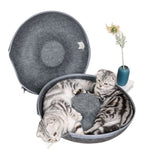 Dark gray felt donut cat bed unzipped to show the circular interior, with two cats resting inside.