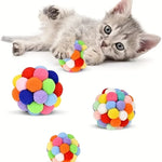 Gray kitten beside colorful pom-pom cat toy balls on a white background