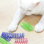 Cat pawing a green plastic spring toy beside colorful spare springs