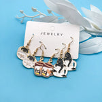 Three pairs of teacup cat fashion earrings beside white leaves